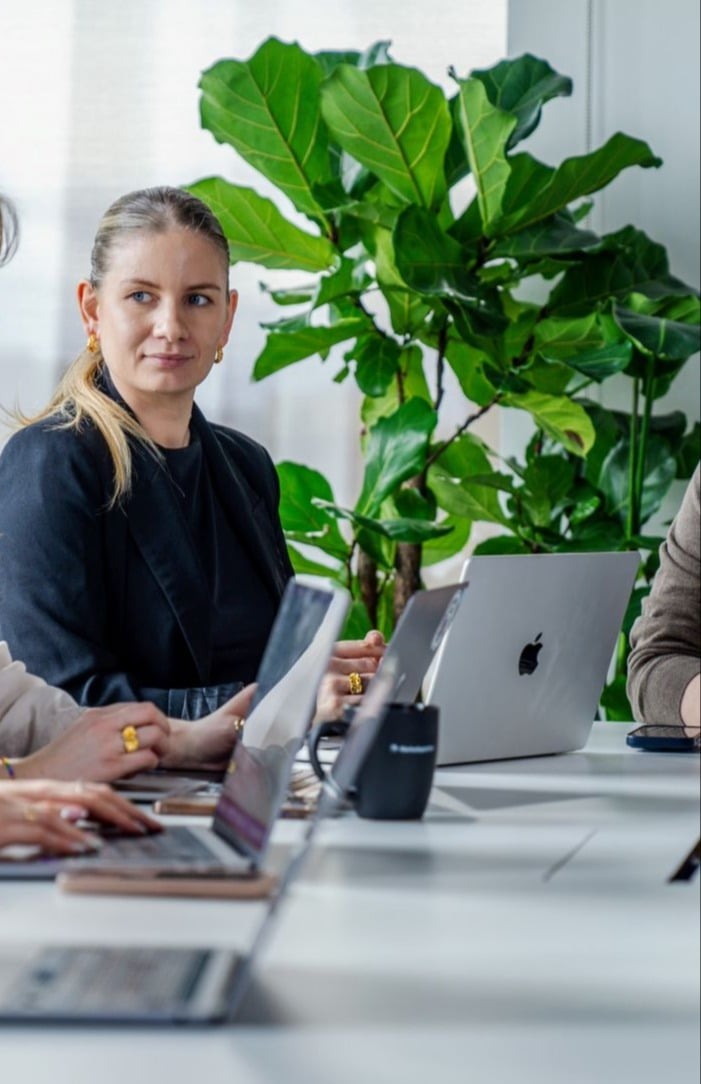 Intuvio-ansatt som sitter ved bord foran PC med grønn plante i bakgrunnen